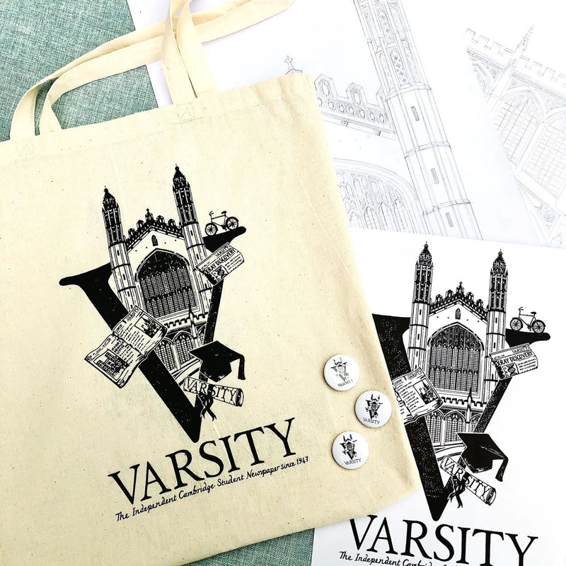 Natural canvas tote bag with Varsity monogram design and text, surrounded by matching badges. Original pencil sketch on table in background.